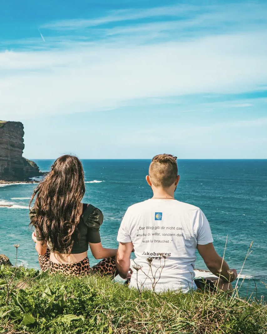 Rigina und Andreas sitzen auf einer Klippe und blicken aufs Meer